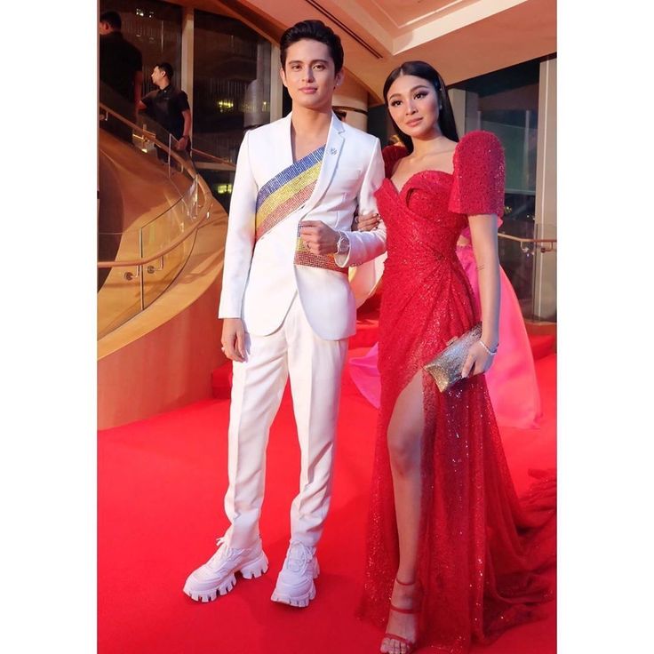 a man and woman in formal wear posing for the camera on a red carpeted area