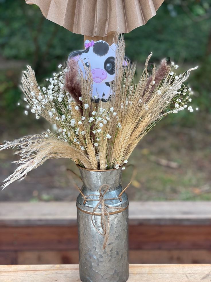 a vase filled with dried flowers and a stuffed cow in it's centerpiece