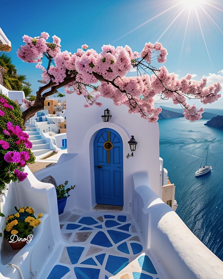 a blue and white house with flowers on the balcony overlooking the water in front of it