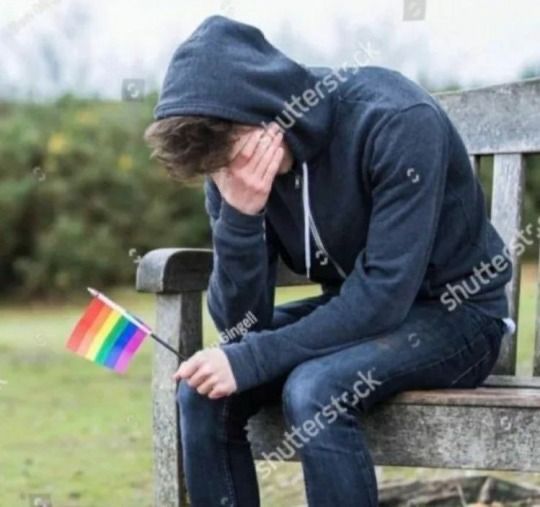 a man sitting on a bench with his head in his hands and holding a rainbow flag