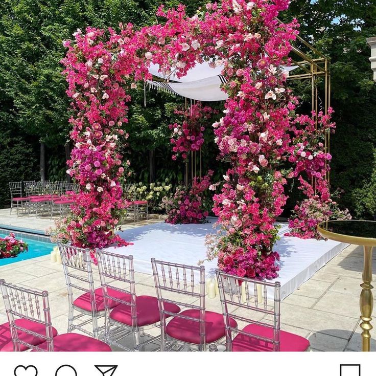 an outdoor wedding setup with pink flowers and white linens on the ground, in front of a swimming pool