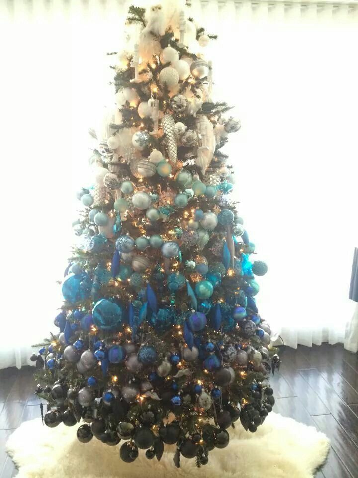 a christmas tree is decorated with blue and silver ornaments on it's sides, along with a white rug