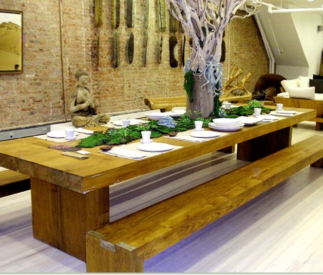 a wooden table with plates and bowls on it in front of a large brick wall