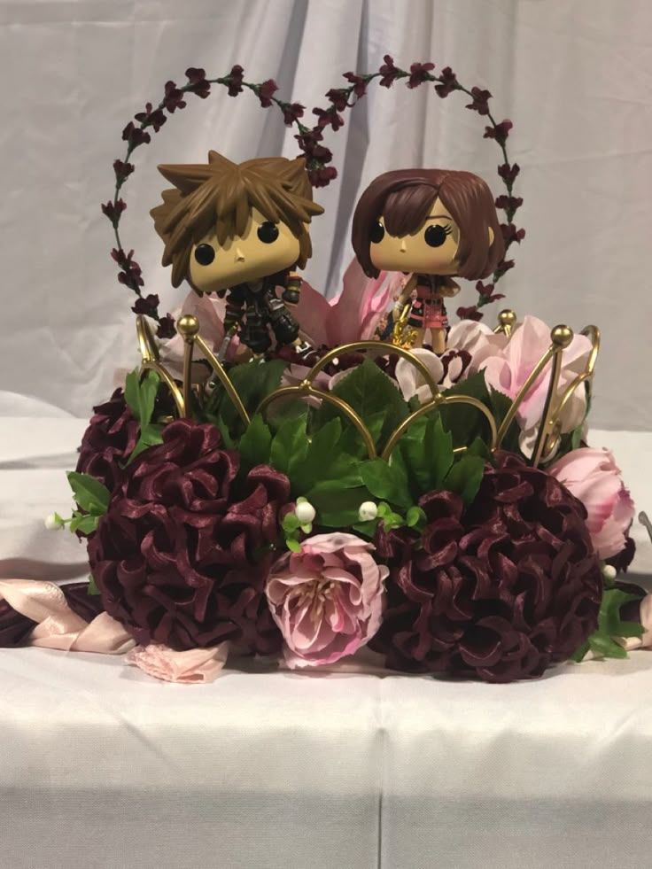 two figurines sitting on top of a flower arrangement