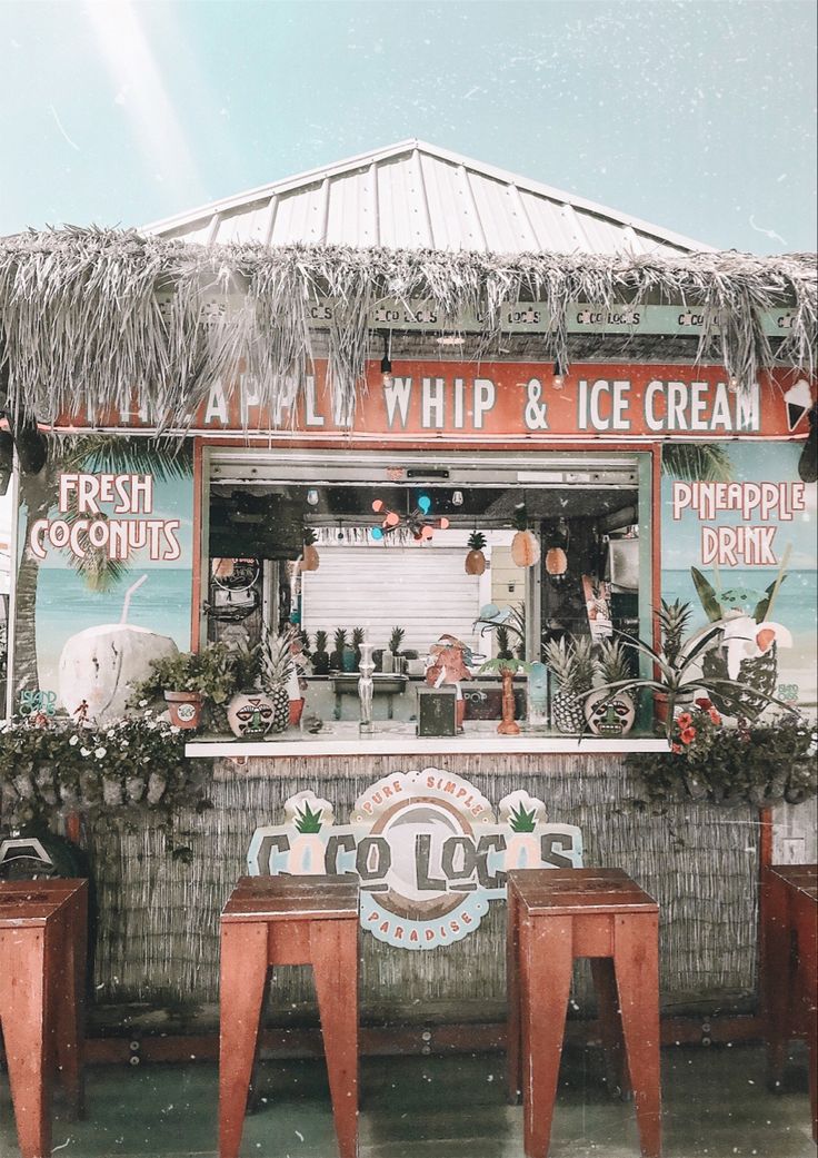 an ice cream stand with two stools in front of it and a tiki bar behind it