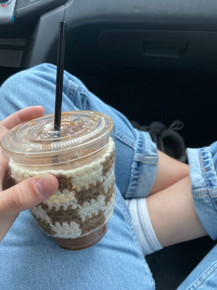 a person holding a drink in their hand while sitting on the floor next to a car