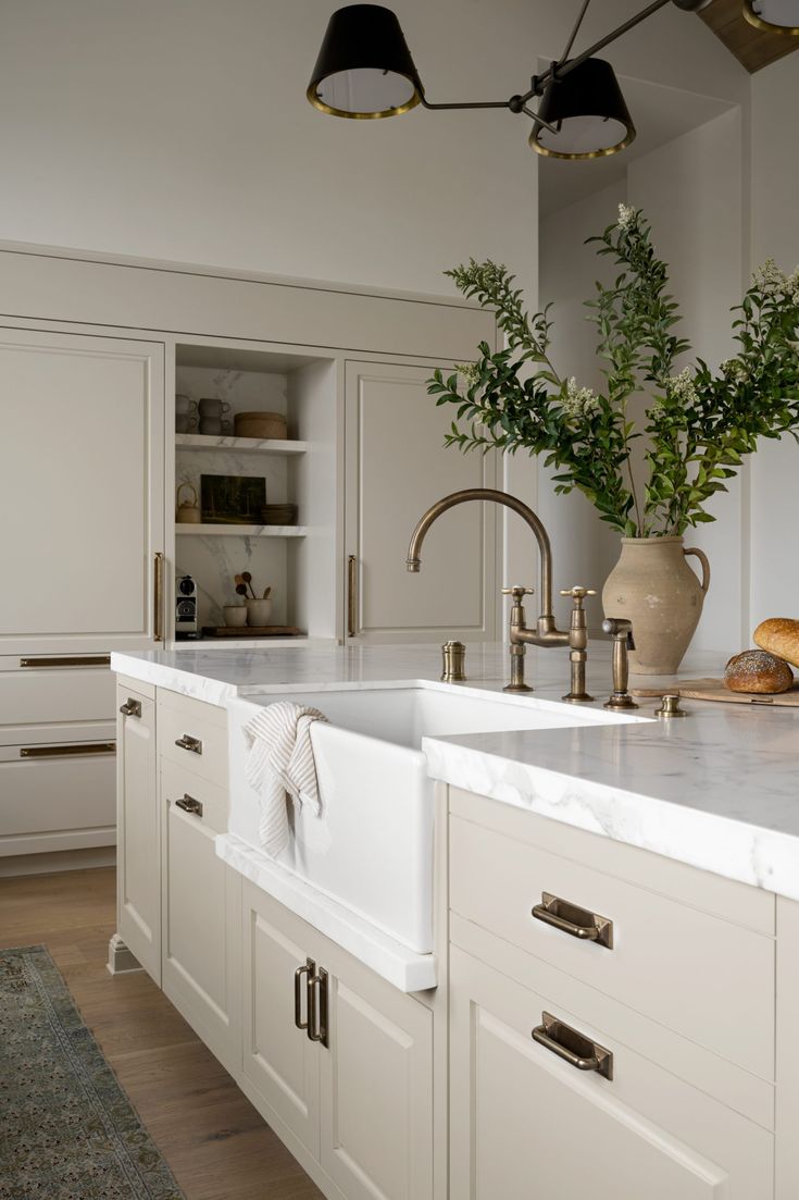 a kitchen with white cabinets and marble counter tops, gold faucets and green plants