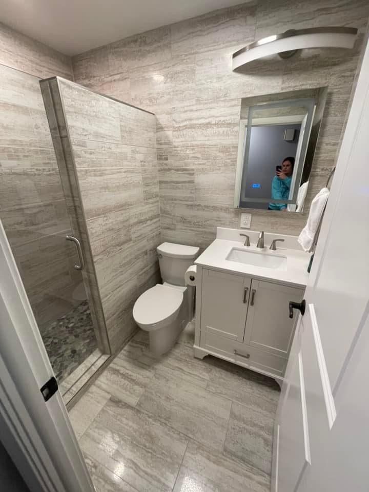 a white toilet sitting under a bathroom mirror next to a walk in shower and sink