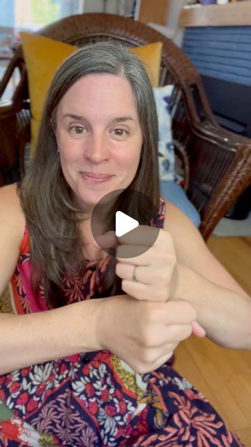 a woman sitting on top of a wooden floor holding an object in one hand and pointing at the camera