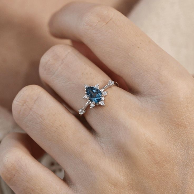 a woman's hand with a blue diamond ring on her left hand and the other hand holding an engagement ring