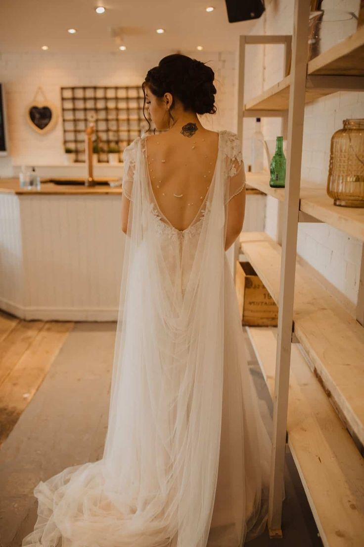 the back of a woman in a wedding dress looking at shelves with items on them