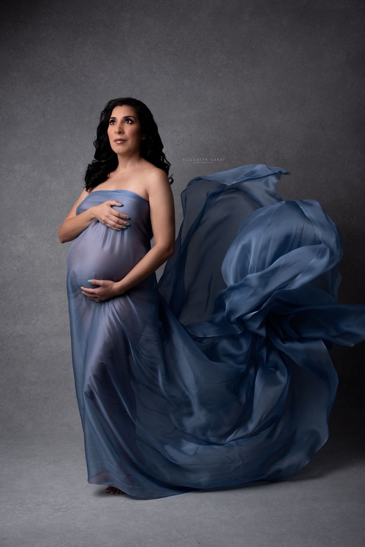 a pregnant woman in a blue dress posing for the camera with her flowing fabric behind her