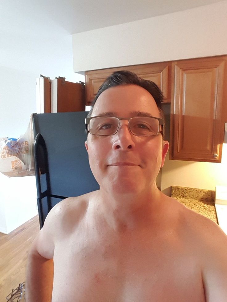 a shirtless man wearing glasses is taking a selfie in the kitchen with his refrigerator