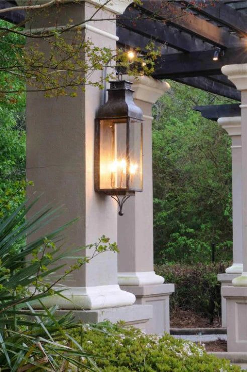 a lantern hanging from the side of a pergolated covered patio with trees in the background