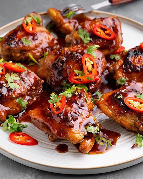 a white plate topped with chicken wings covered in sauce and garnished with red peppers