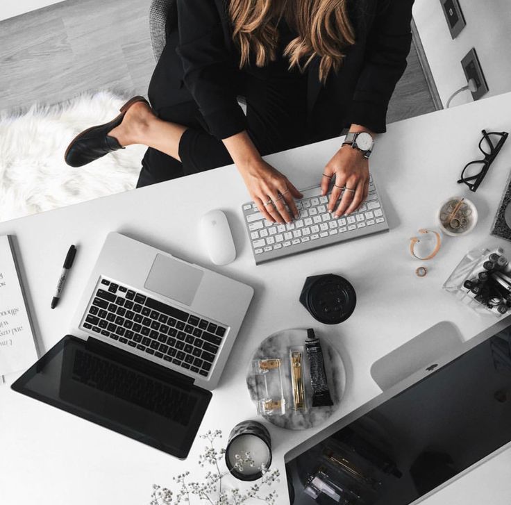 a woman sitting at a desk typing on a laptop computer, surrounded by other office supplies