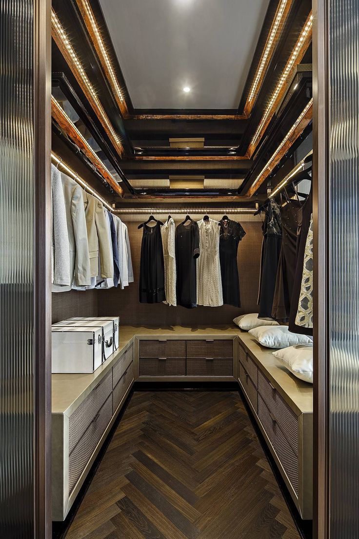 a walk in closet with clothes hanging on the walls and wooden flooring, along with drawers