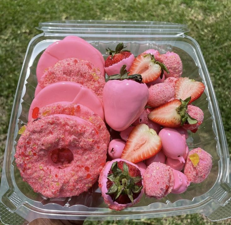 a plastic container filled with donuts covered in pink frosting and strawberries on top of it