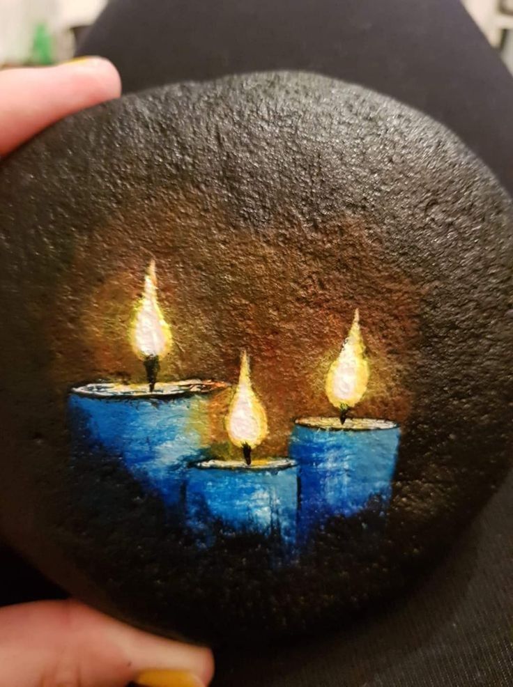 a person holding up a painted rock with three candles on it