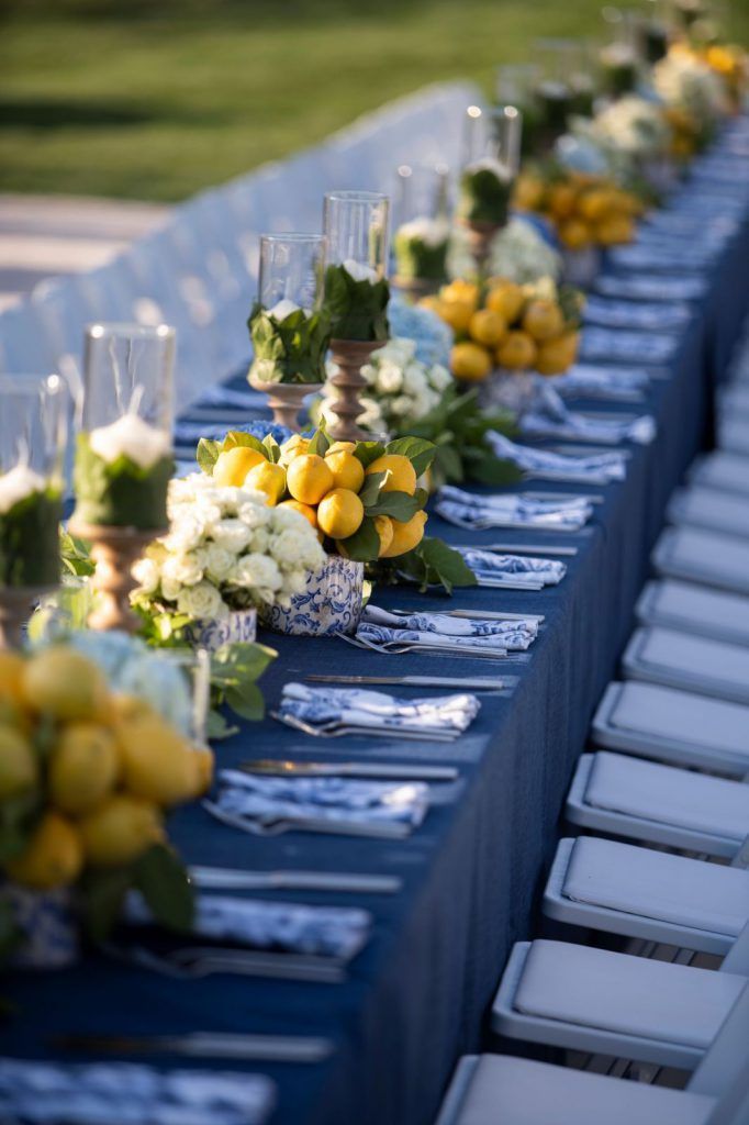 a long table is set up with blue linens and lemons for the centerpieces