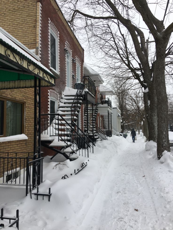 a snow covered sidewalk next to a brick building with stairs and railings on both sides