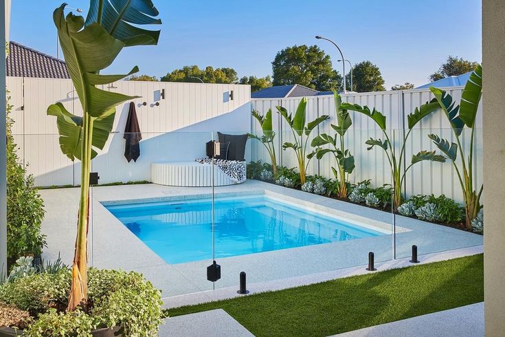 an outdoor swimming pool surrounded by greenery and plants in the back yard, next to a white fence