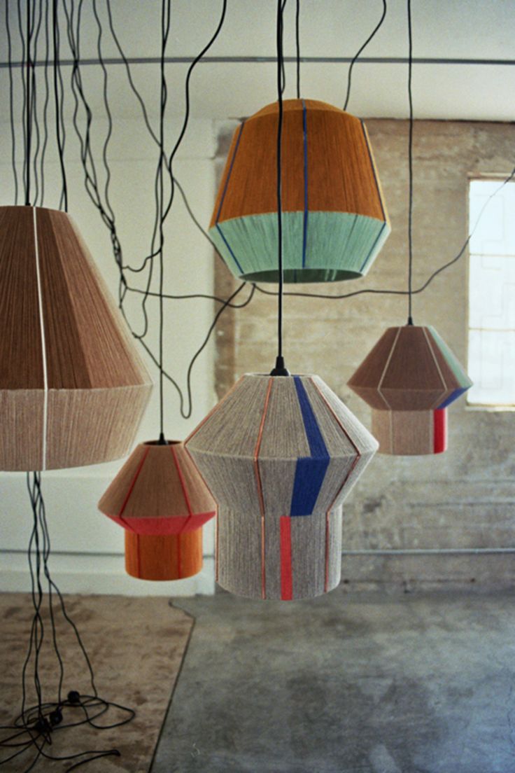 several multicolored lamps hanging from wires in a room with concrete walls and windows