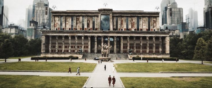 people are walking around in front of a large building with many windows and statues on it