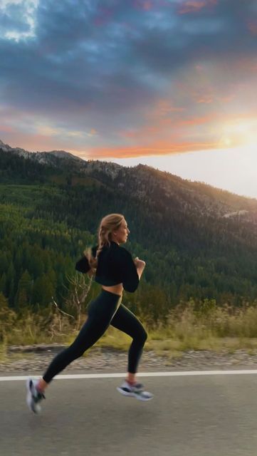 a woman running down the road with mountains in the background