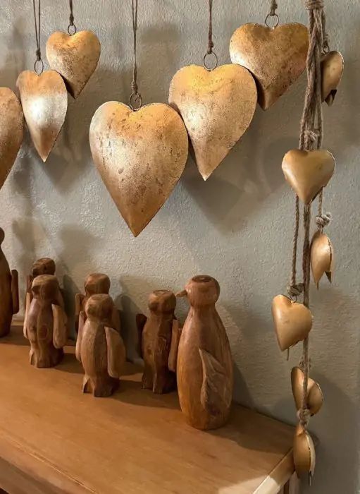 several wooden hearts hanging from hooks on a wall above a mantle with figurines in the shape of animals