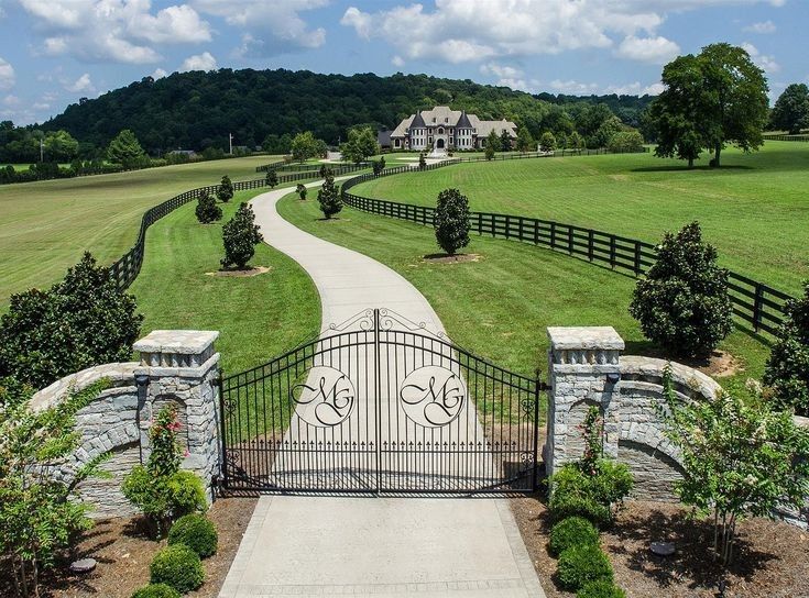 a driveway leading to a gate in the middle of a lush green field