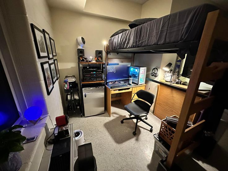 a room with a bed, desk and computer equipment in the corner on the floor