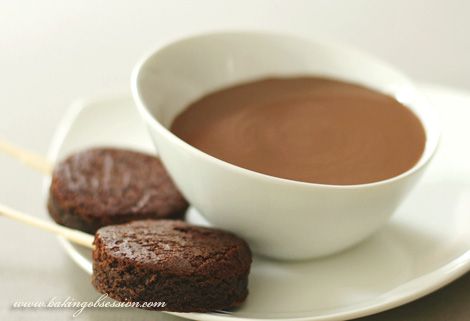 two chocolate cookies on a plate next to a cup of hot chocolate with sticks sticking out of it