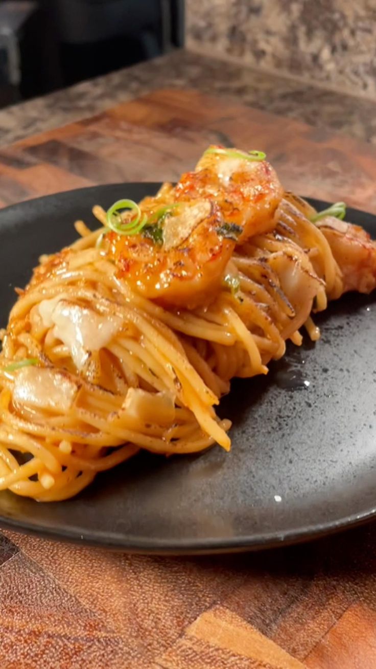 a black plate topped with pasta and shrimp