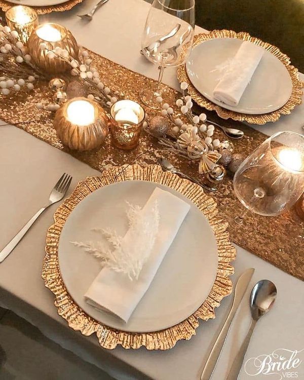 the table is set with white and gold plates, silver cutlery, and candles