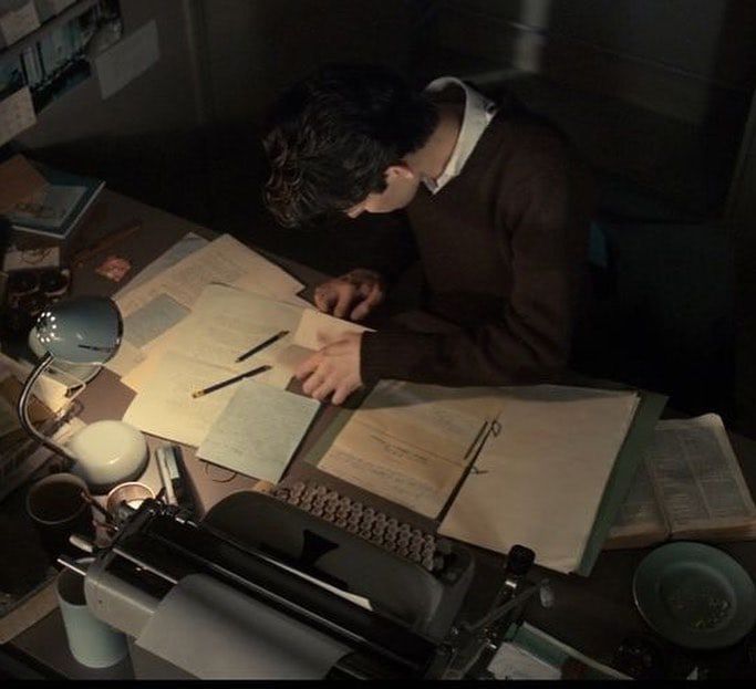 a man sitting at a desk with an old typewriter in front of him and writing on paper