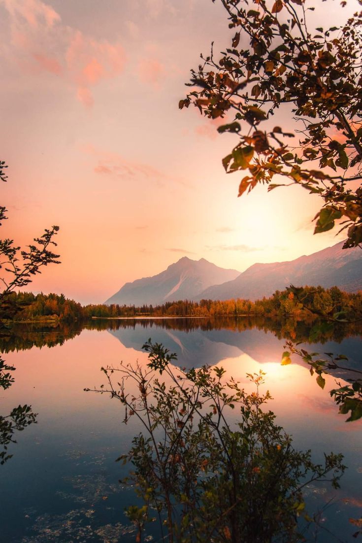 the sun is setting over a lake with mountains in the background