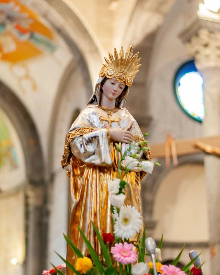 a statue of the virgin mary holding flowers in front of a church alter with stained glass windows