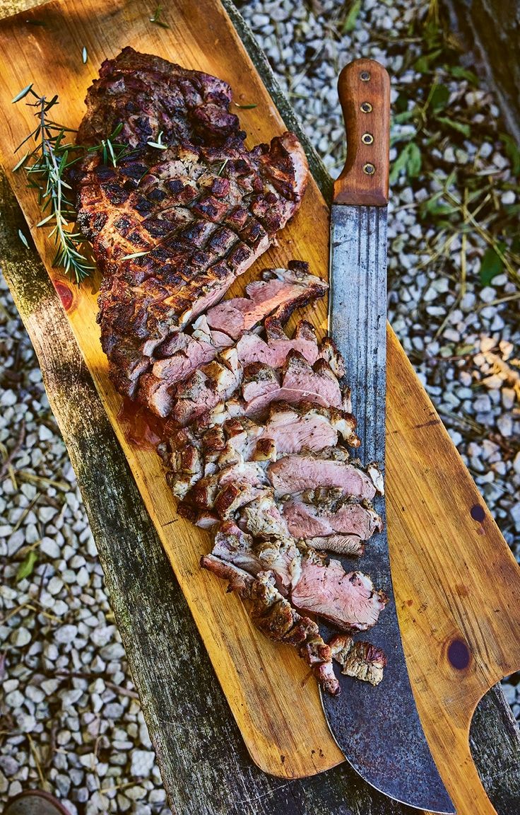 sliced meat sitting on top of a wooden cutting board next to a knife and fork