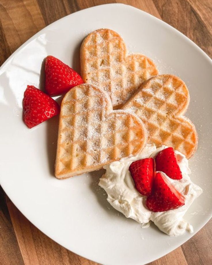 three heart shaped waffles with whipped cream and strawberries on a white plate