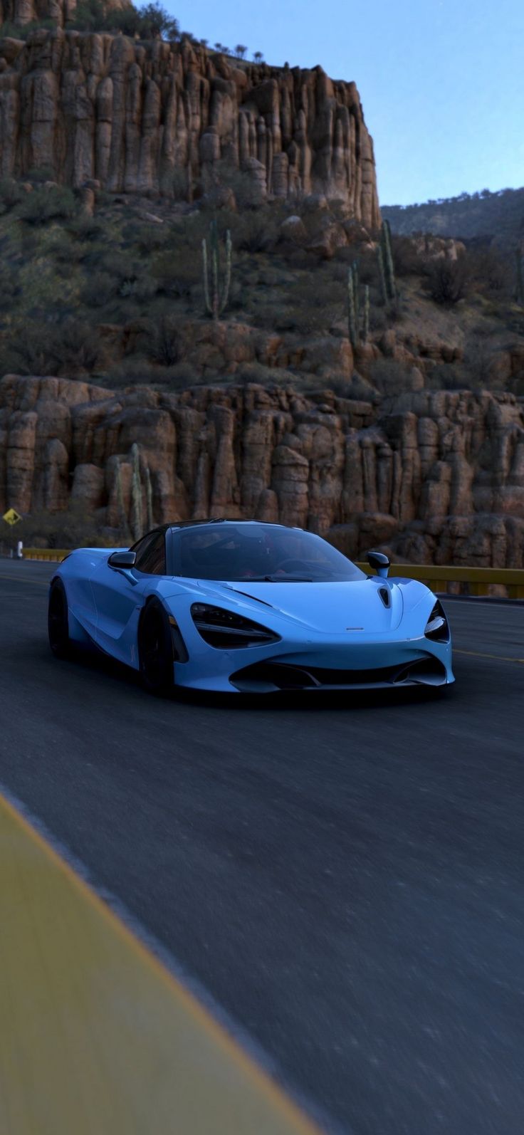 a blue sports car is driving down the road in front of some mountains and rocks