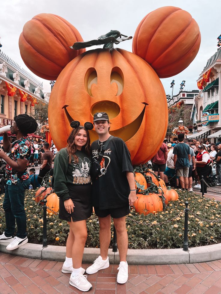 two people standing next to each other in front of a mickey mouse pumpkin