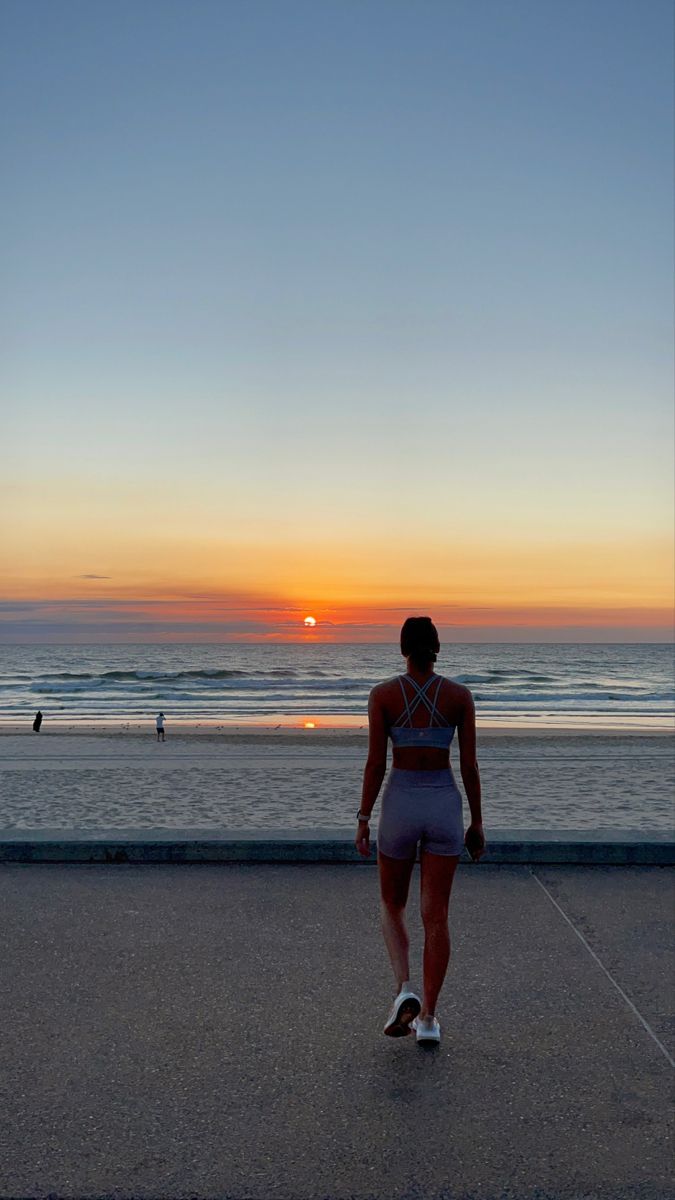 a woman walking on the beach at sunset