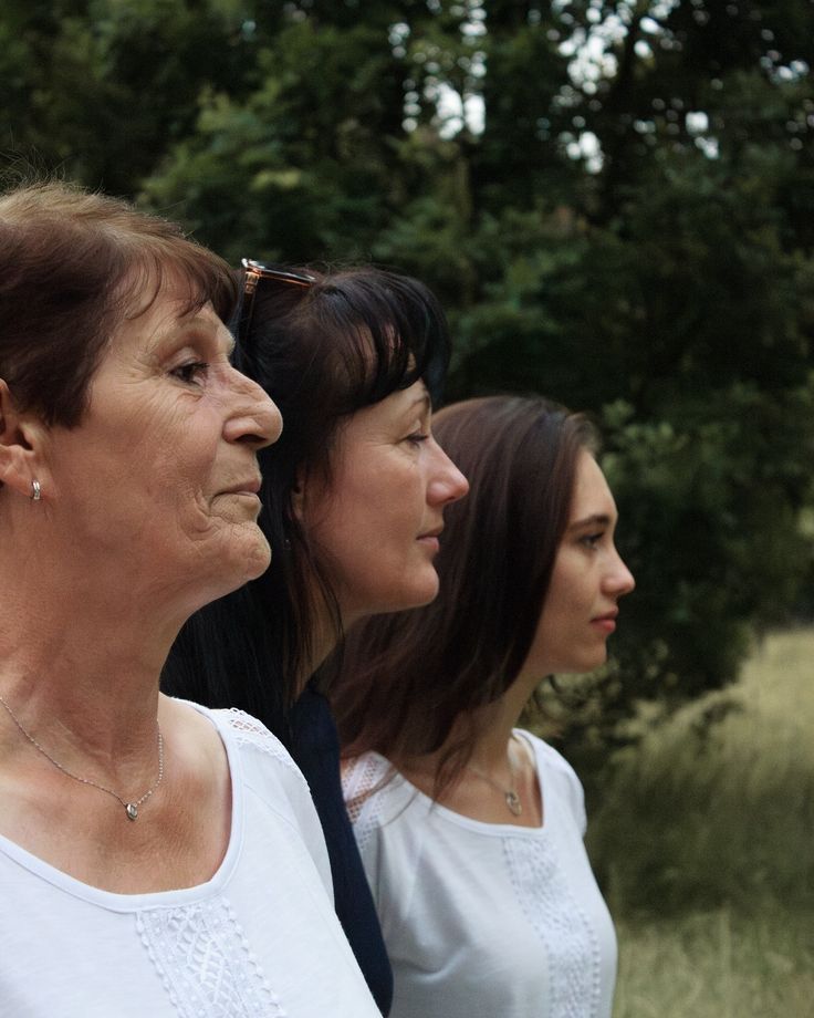 three women standing next to each other with trees in the background