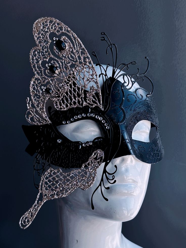 This glittering mask takes on the shape of a butterfly, symbolizing transformation and grace. The striking contrast of black and silver exudes an air of opulence and charm, while shimmering rhinestones adorn the mask. Whether you're attending a grand masquerade ball or a themed gala this mask ensures you'll be the center of attention. Age Group/Gender - Adult/Women Size/Type - One size fits all adults Mask Color - Black/Silver Mask Material - Polyresin and laser cut metal Masquerade Mask With Glasses, Masquerade Mask Design, Masquerade Mask Silver, Butterfly Masquerade Mask, Butterfly Masquerade, Mask Butterfly, Vampire Mask, Black Masquerade, Black Masquerade Mask