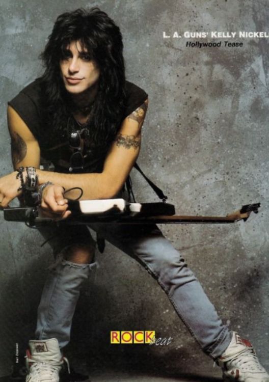 a man with long hair and tattoos sitting on a skateboard holding an electric guitar