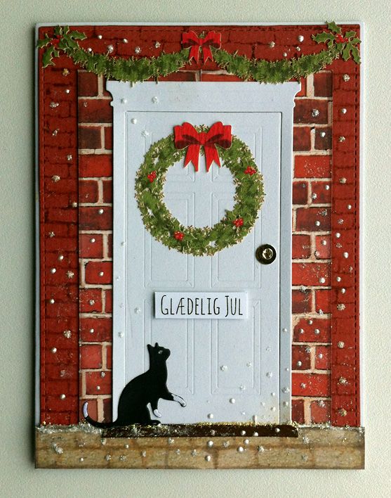 a cat sitting in front of a white door with a wreath on it's side