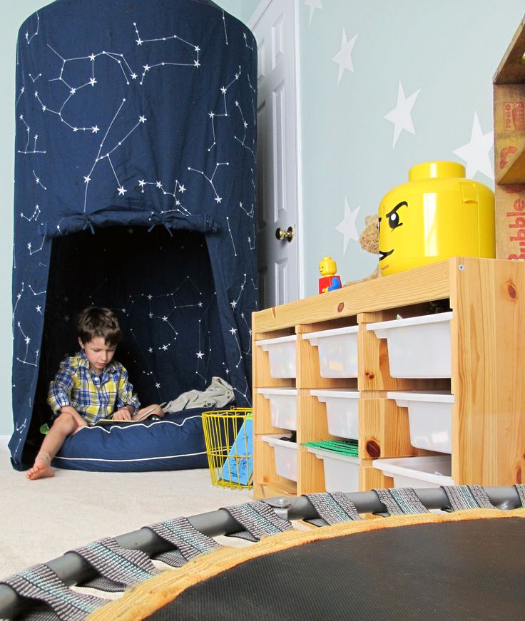 a young boy is sitting in his play room with a blue tent and white stars on the wall