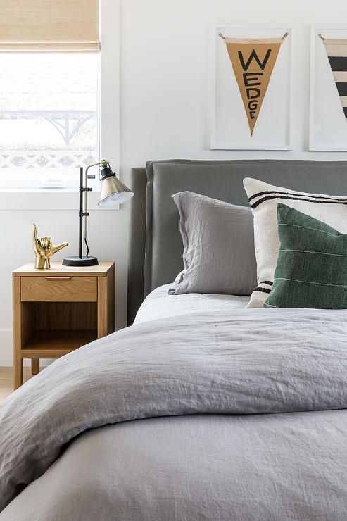 a bed with grey linens and pillows in a white room next to two pictures on the wall