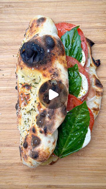 a piece of pizza with tomatoes, cheese and spinach on it sitting on top of a wooden cutting board